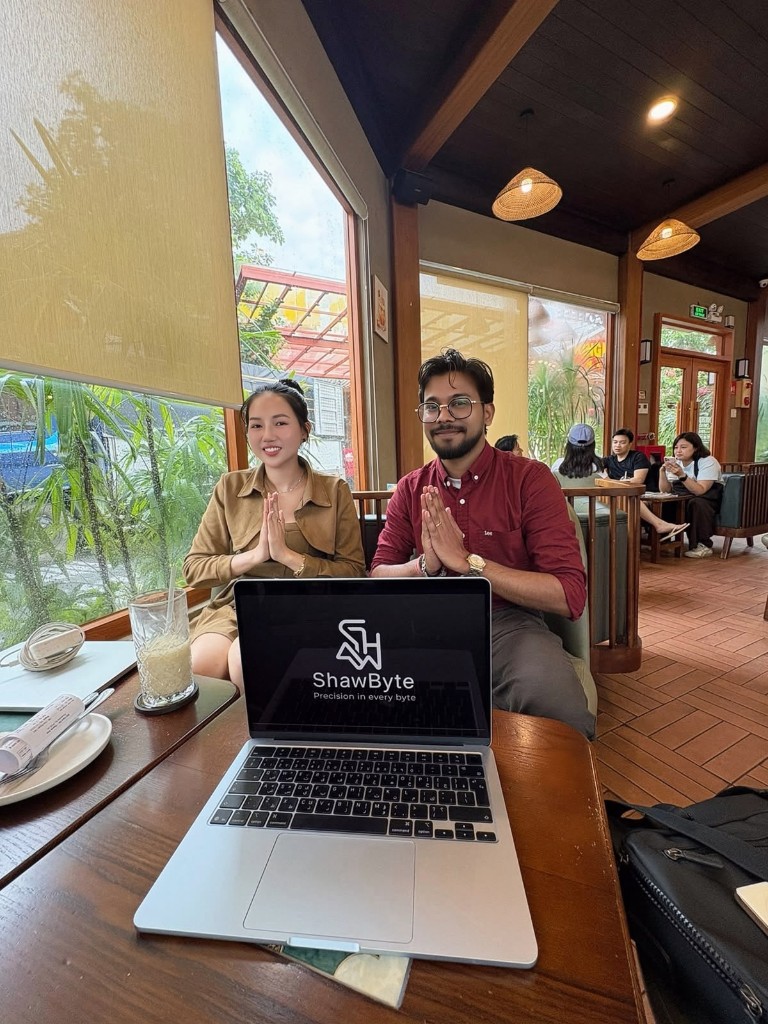Nguyễn Việt Trinh with Rajendra Kumar Shaw greeting with a Namaste at a café in Phu Quoc, a laptop showing ShawByte in front of them